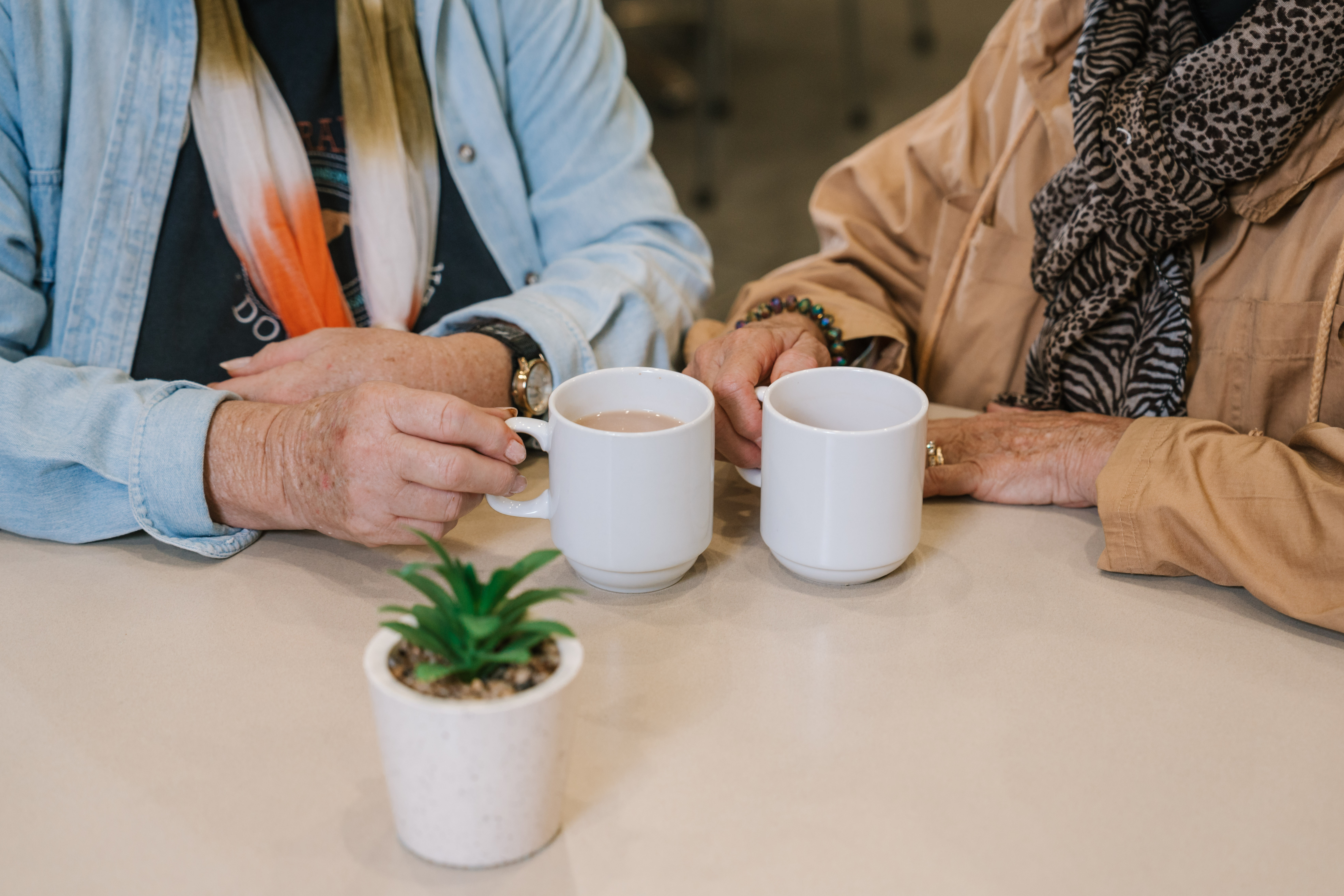 Two people sit together at a table holding mugs of coffee, suggesting a relaxed and supportive conversation during a peer support group meeting.